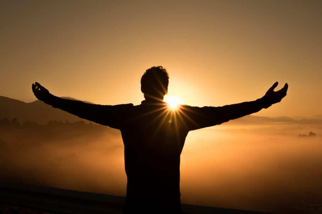 Silhueta de um homem com os braços abertos em frente ao pôr do sol