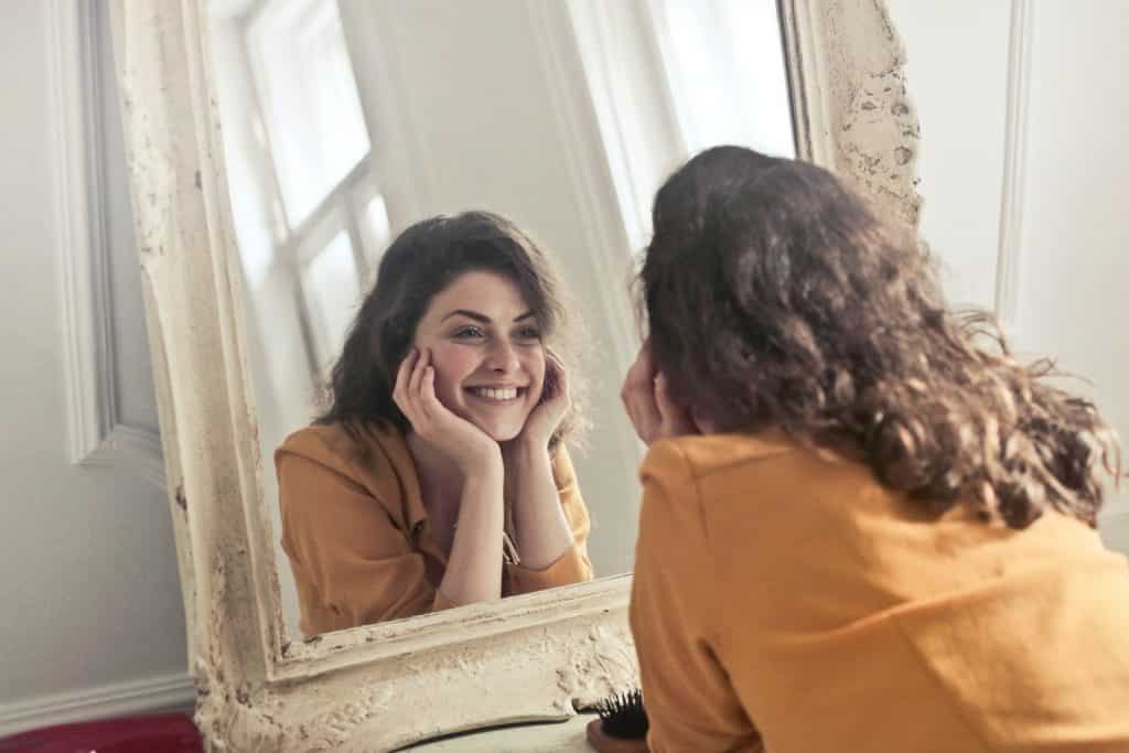 Mulher sorri enquanto olha para seu reflexo no espelho.