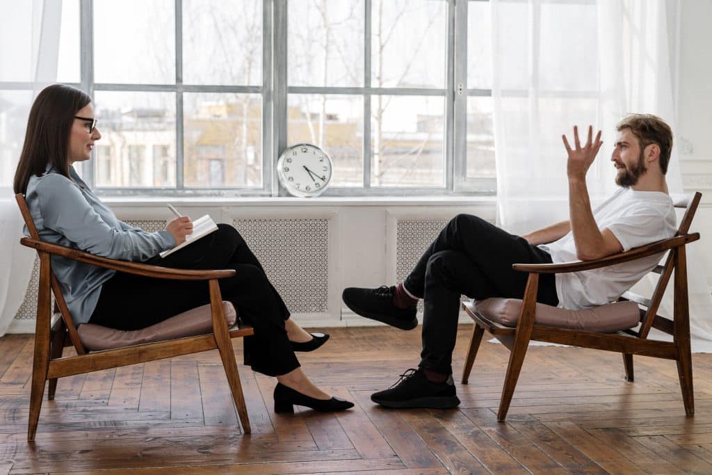 Homem sentado em uma cadeira conversando com psicologa a sua frente