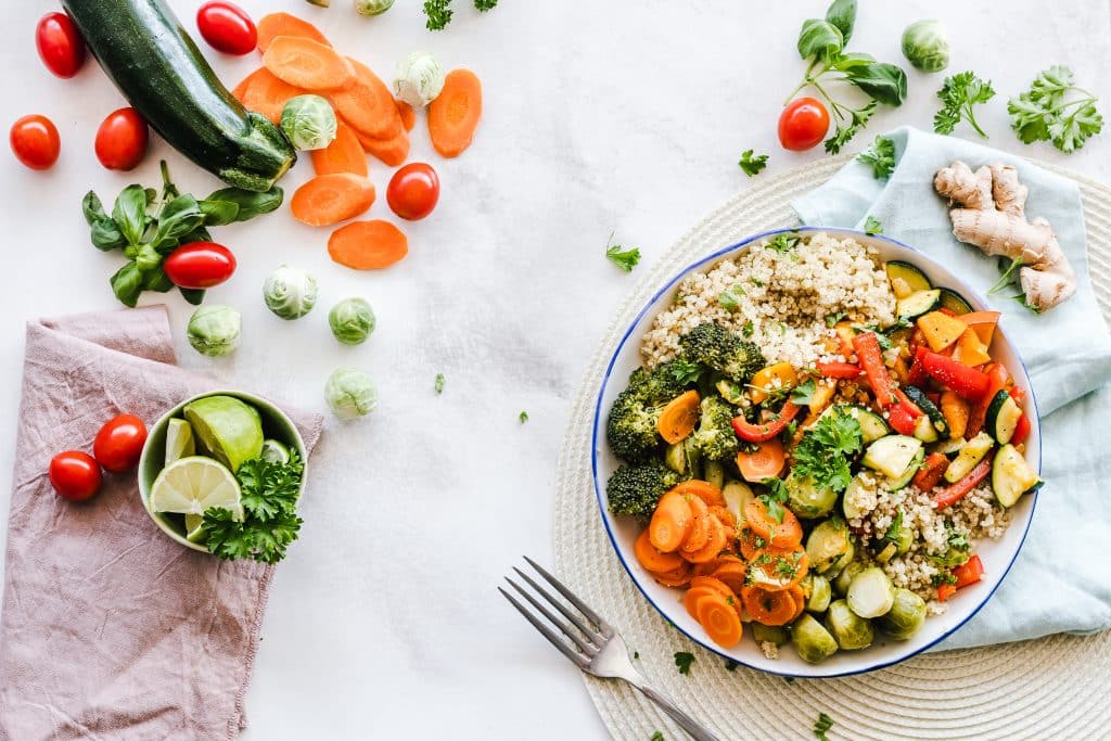 Bowl com legumes, grãos e verduras sobre uma mesa, ao lado de um garfo.