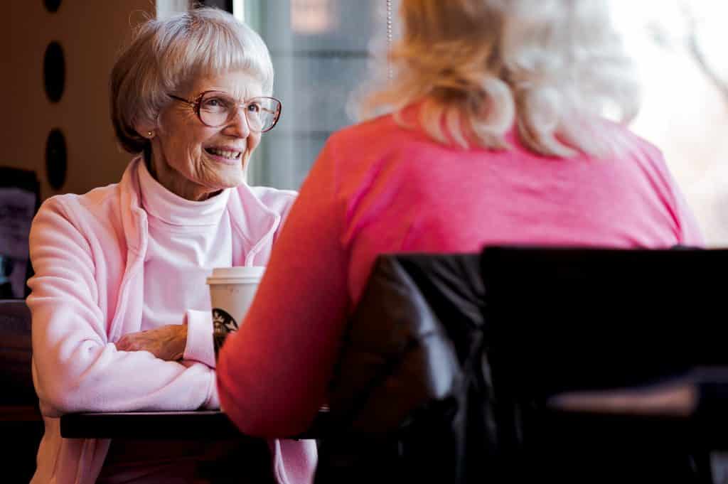 Duas mulheres idosas sentadas à mesa de um restaurante, sorrindo e conversando.