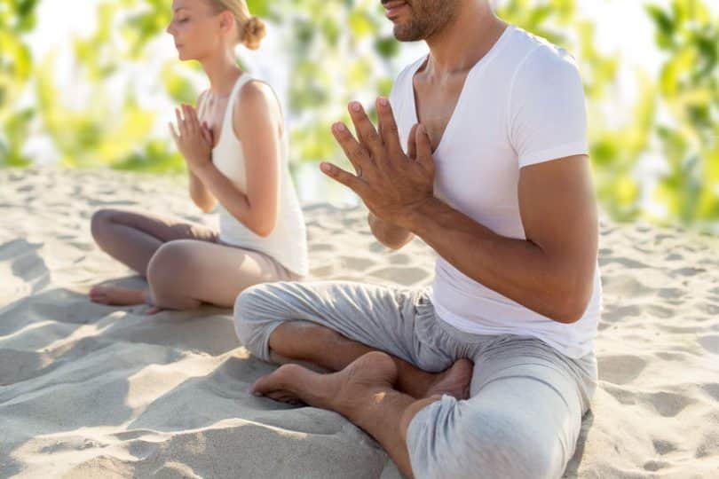 Duas pessoas sentadas na areia, de pernas cruzadas, meditando.