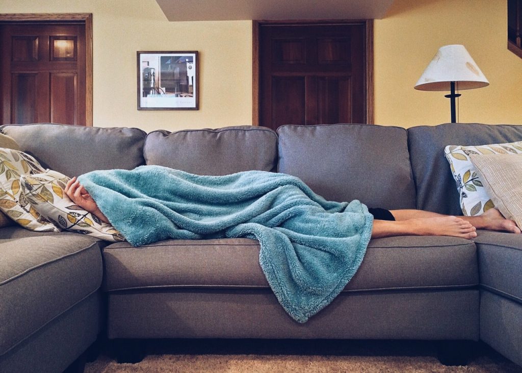 Pessoa deitada no sofá sob uma coberta.