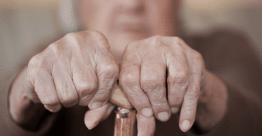 Mãos de pessoa idosa segurando muleta.