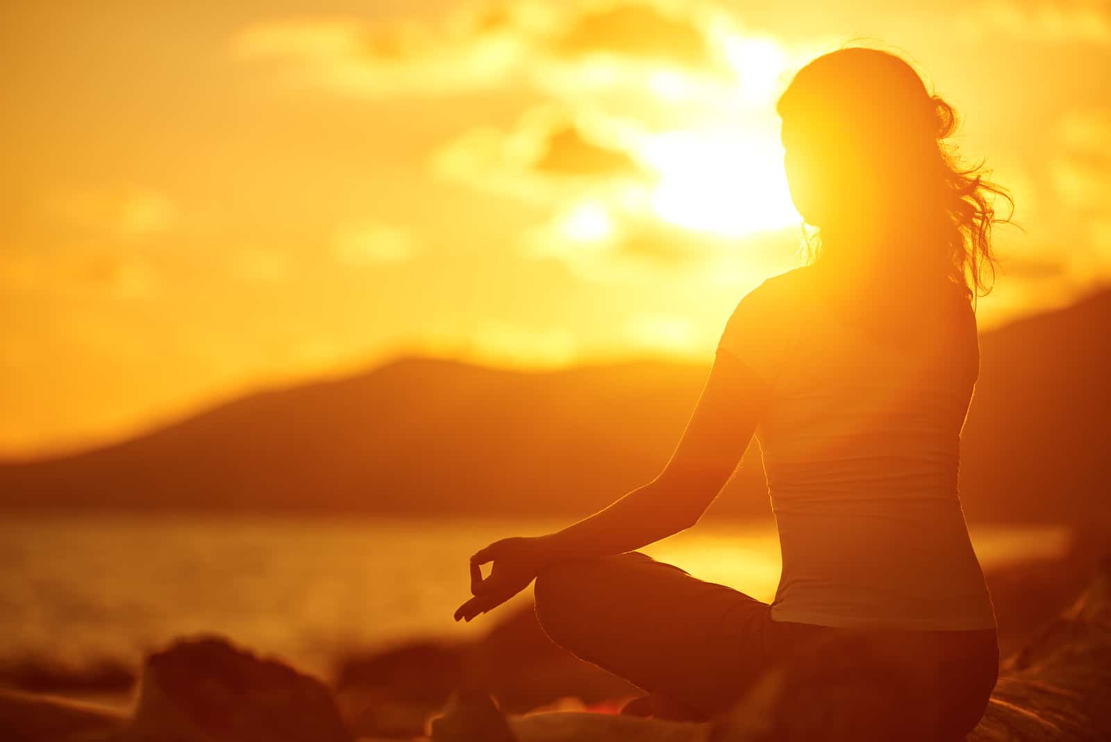 Woman Meditating In Lotus Pose On The Beach At Sunset