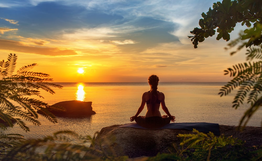 Mulher sentada em uma pedra meditando enquanto o sol nasce