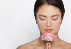 Mulher asiática com os olhos fechados segurando flor rosa.