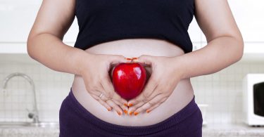 Mulher grávida segurando uma maça vermelha em frente da sua barriga.