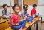 Crianças em posição de meditação em cima de suas mesas escolares.