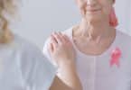 Mulher apoiando o braço sobre o ombro de uma mulher mais velha, com lenço na cabeça, que sofre de câncer de mama.