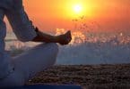 mulher praticando ioga perto do mar ao pôr do sol