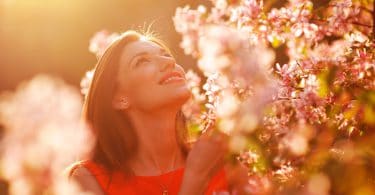 Mulher jovem e sorridente observando as flores em um jardim num dia ensolarado.