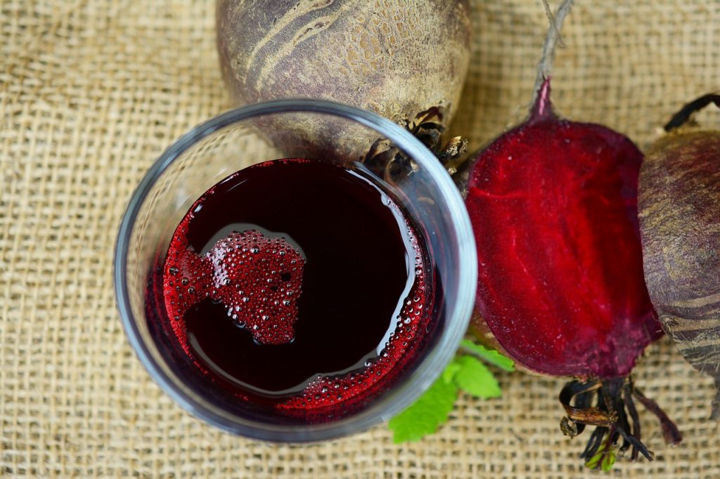 Suco de beterraba em um copo de vidro, com beterrabas cruas ao lado.