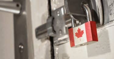 Porta trancada com fechadura de ferro, presa com um cadeado com a bandeira do Canadá.