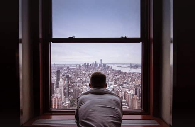 Homem de costas em janela com vista para cidade
