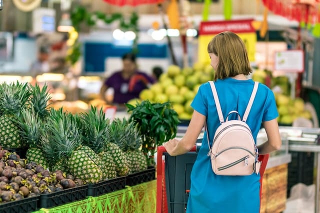 Mulher de costas andando no supermercado escolhendo frutas