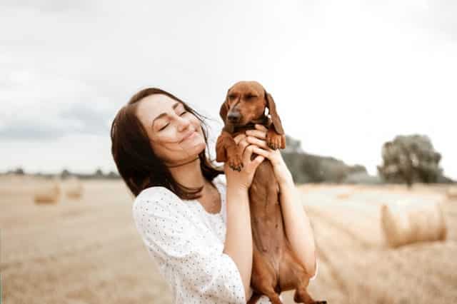 Mulher com cachorro nas mãos de olhos fechados sorrindo