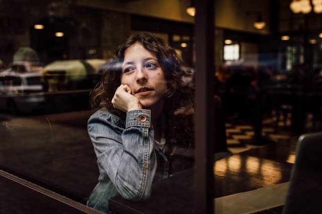 Mulher em mesa restaurante com braço apoiado na janela vista do lado de fora pelo vidro