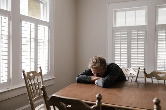 Homem apoiado na mesa sozinho com janelas fechadas