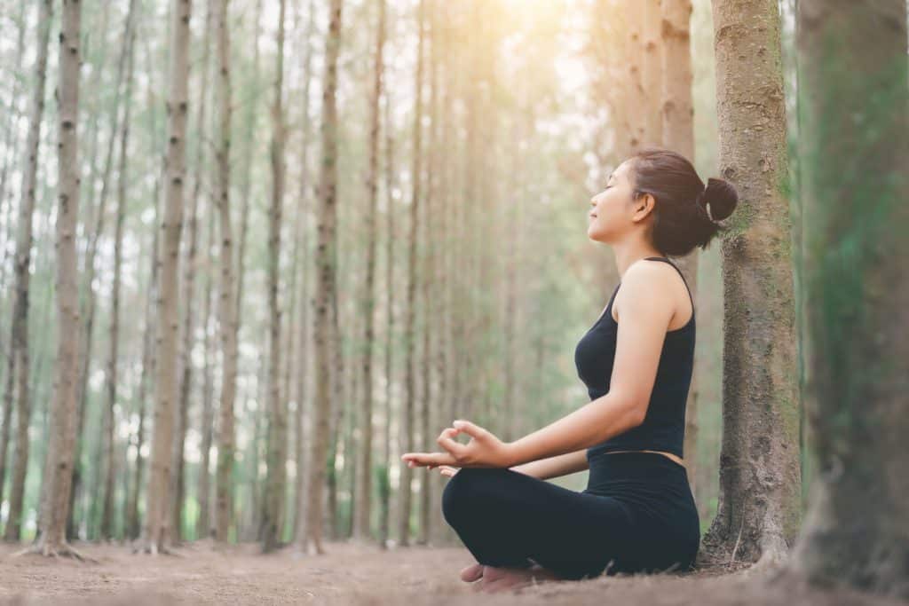 Mulher sentada em uma floresta meditando.