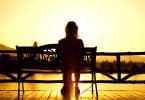 Mulher sentada em banco assiste ao pôr do sol.