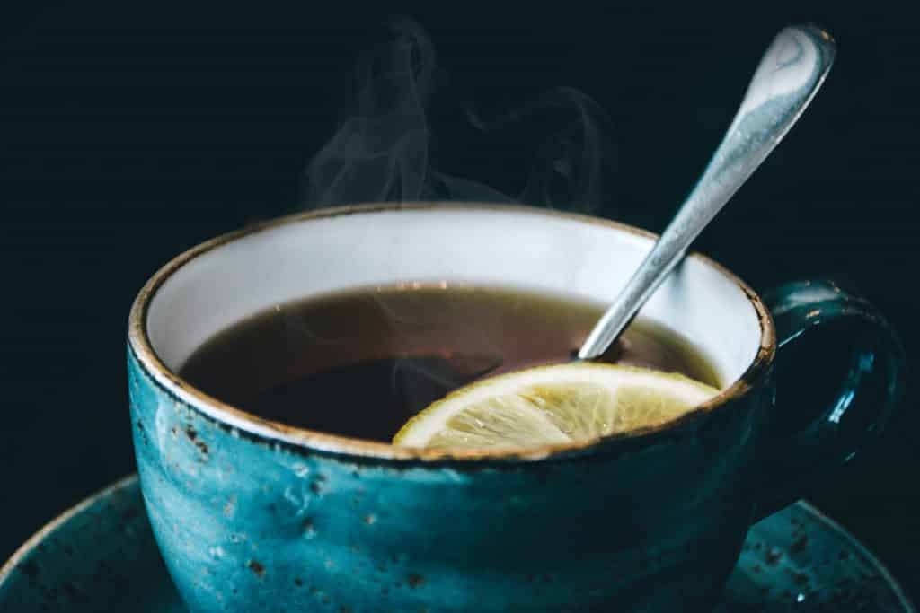 Xícara cheia de chá com uma rodela de limão. Há também uma colher no líquido.
