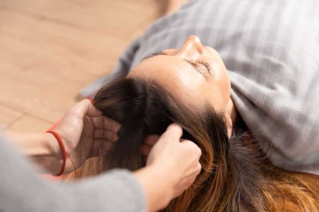 Mulher branca recebendo massagem na cabeça.