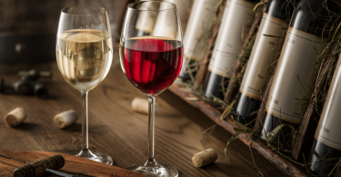 Duas taças de vinho em cima de uma superfície de madeira na qual várias garrafas estão apoiadas