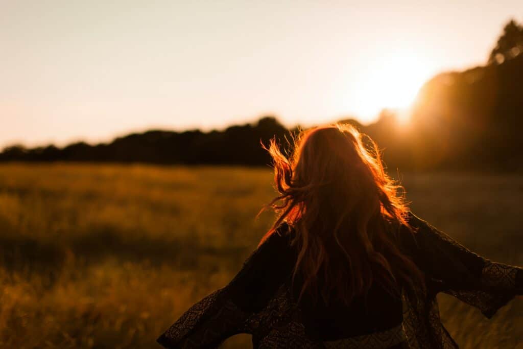 Mulher de costas, com os cabelos esvoaçantes ao pôr-do-Sol.