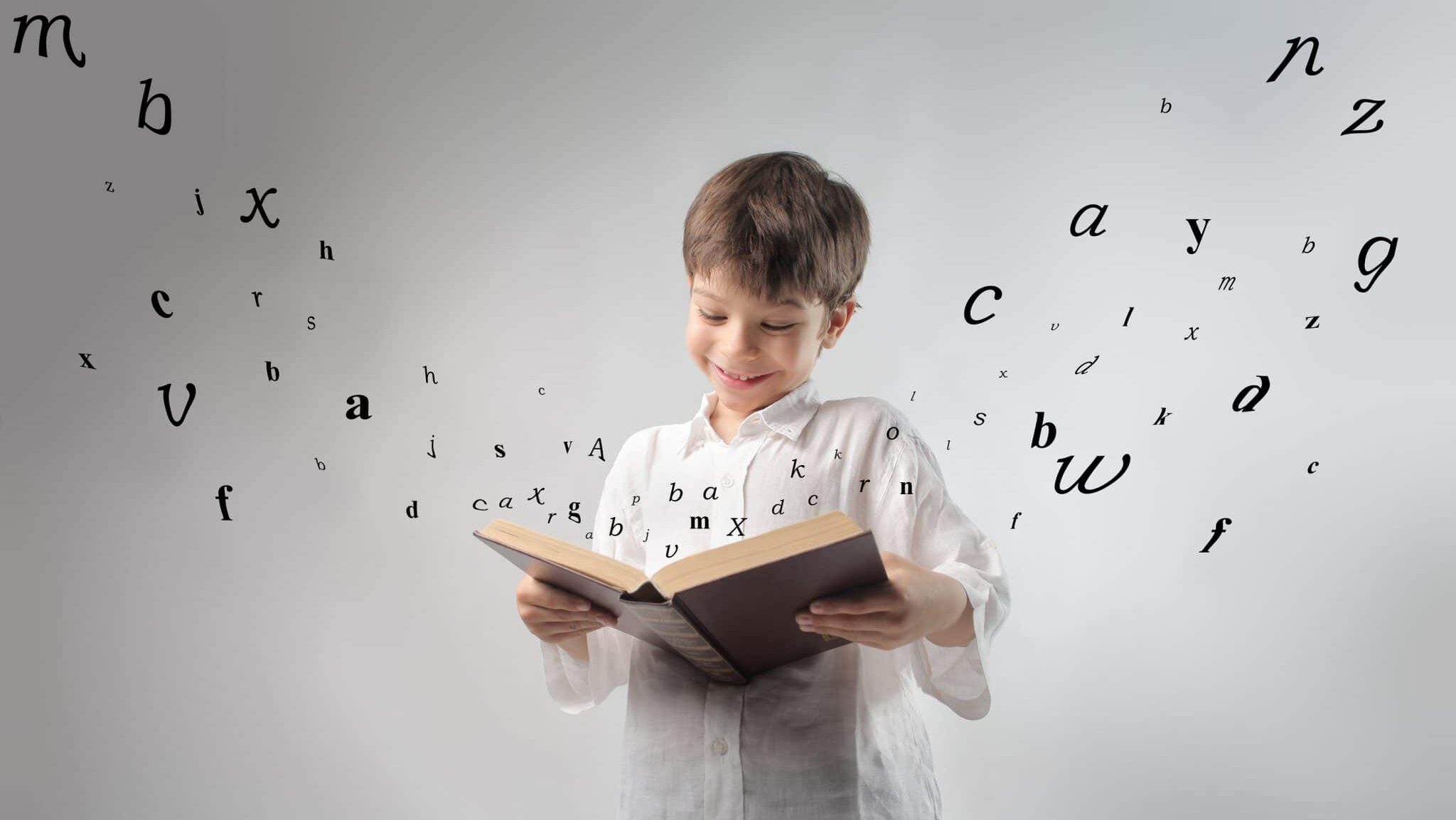 Smiling child reading a book with letters flying away from it