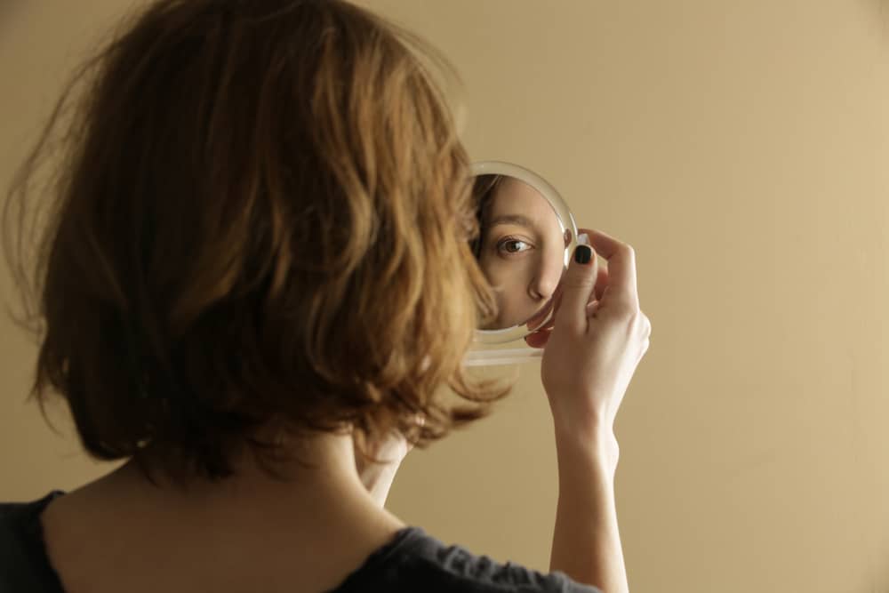 Mulher olhando seu reflexo em um espelho de mão.