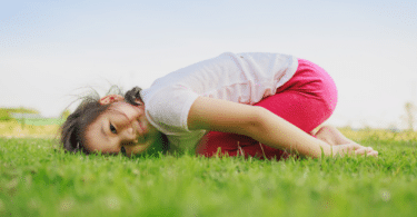 Criança de joelhos e com a cabeça deitada na grama