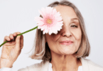 Mulher idosa segurando flor no rosto. Conceito de menopausa.