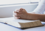 Mãos de mulher sobre a bíblia, juntas, rezando.