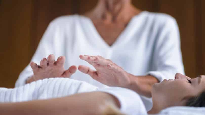 Terapeuta aplica reiki em mulher deitada.