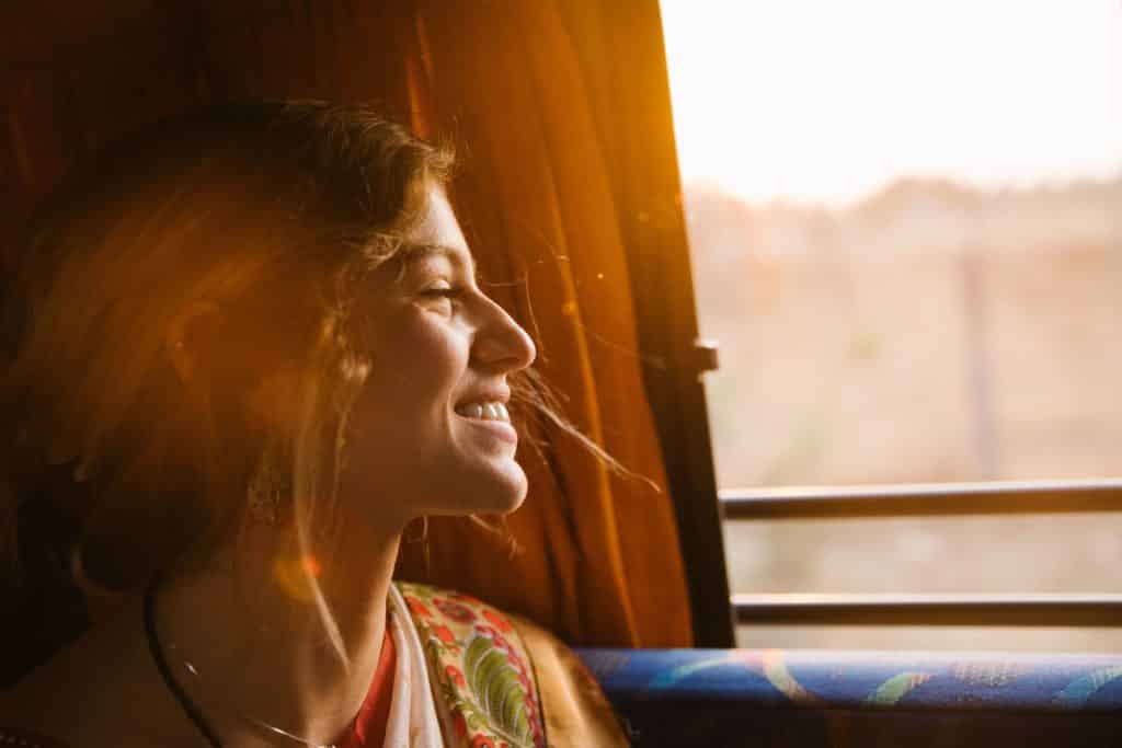 Mulher sorrindo de olhos fechados com o reflexo do sol em seu rosto