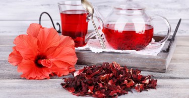 Chá de hibisco em bule de vidro e flor em guardanapo de cor sobre fundo de madeira