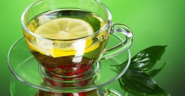 Chá verde em xícara transparente com limão e baga em fundo verde