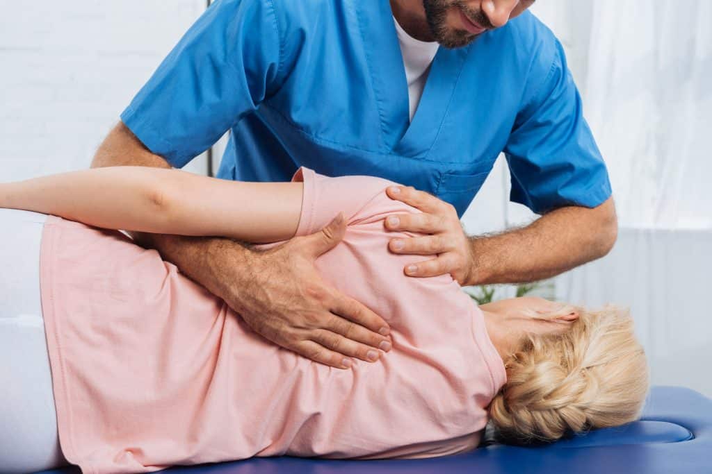 Médico com as mãos nas costas da paciente deitada