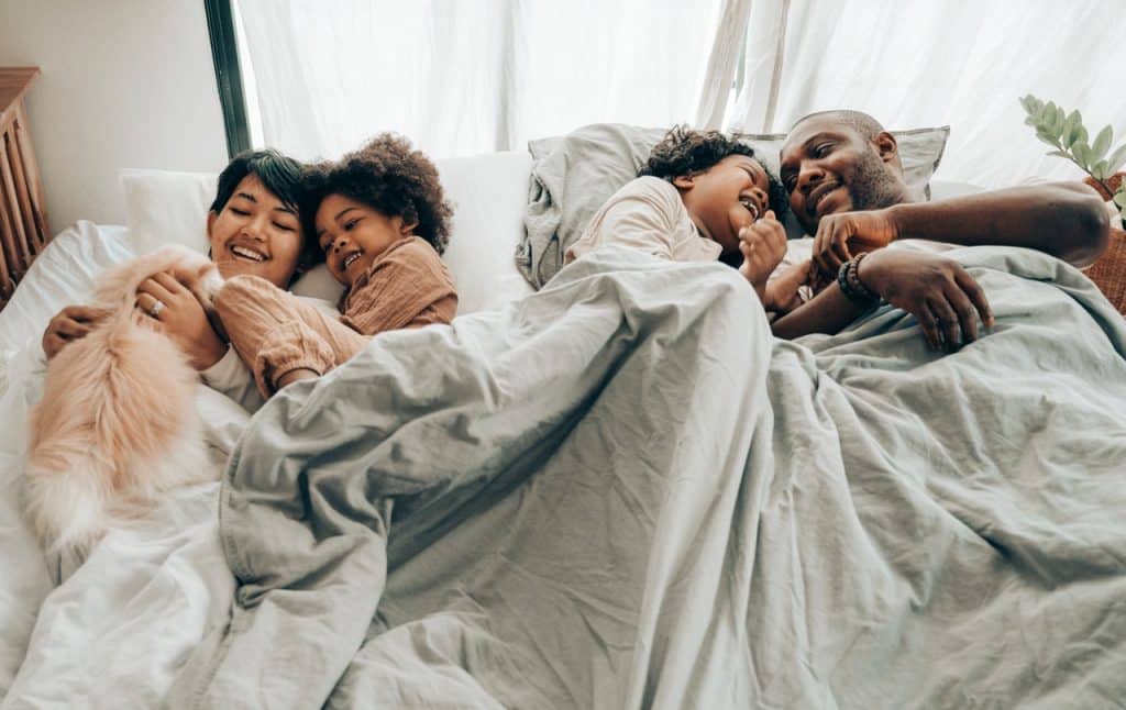 Família de pai, mãe, seus dois filhos e seu gato de estimação deitados em uma cama, juntos.