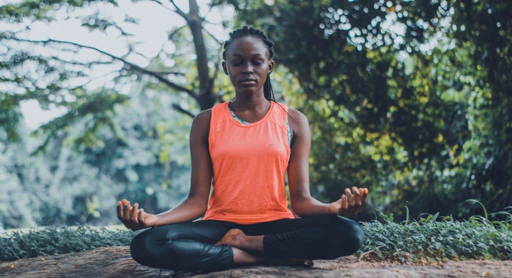 Mulher sentada no chão de um parque natural, meditando ao ar livre.