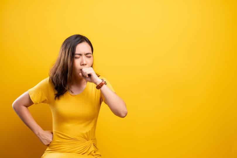 Em cenário amarelo, mulher tosse.