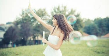 Mulher jovem sorrindo e brincando com bolhas de sabaão em um parque.