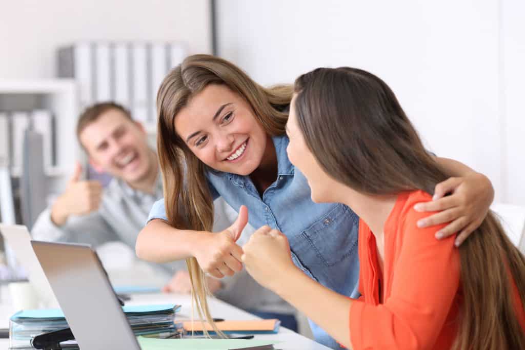 Mulher sorrindo ao receber dois polegares para cima de dois colegas de trabalho.