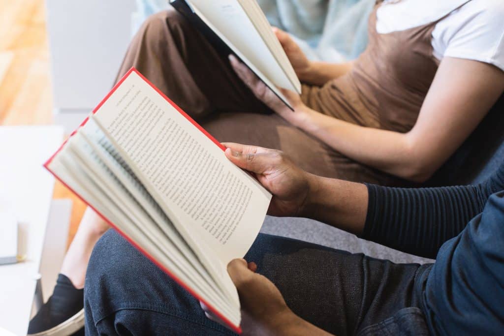 Três pessoas sentadas lado a lado lendo livros em uma sala de espera.