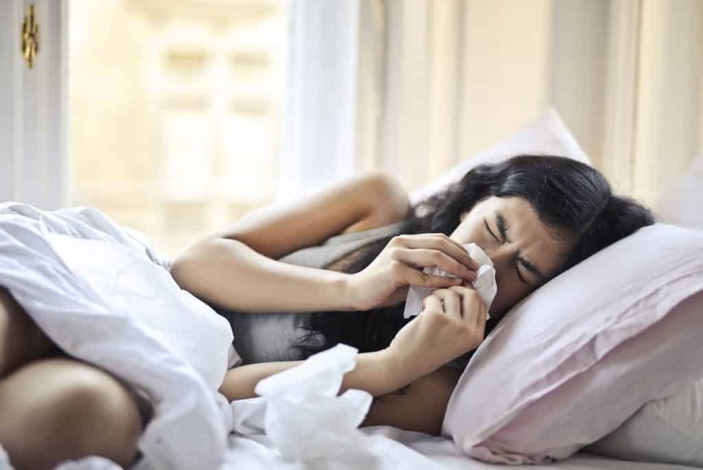 Mulher deitada na cama espirrando em um papel-toalha. 
