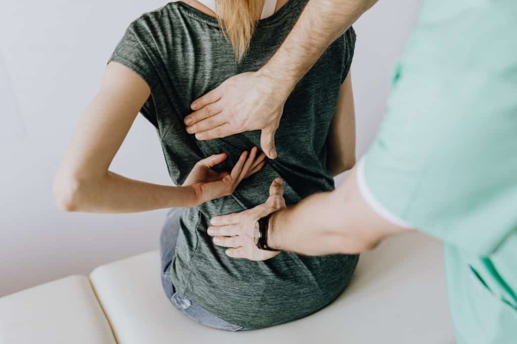 Uma mulher sentada com dores nas costas com um médico analisando. 