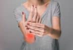 Mulher apertando a mão, em sinal de dor, como sintoma da artrite