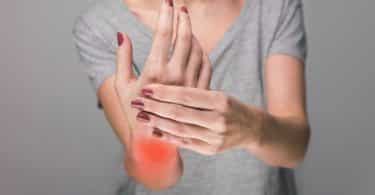 Mulher apertando a mão, em sinal de dor, como sintoma da artrite