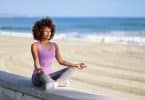 Mulher negra meditando com os olhos fechados na praia.